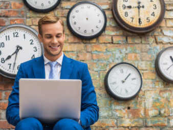 Man,In,Suit,Sitting,Near,Wall,With,Clocks